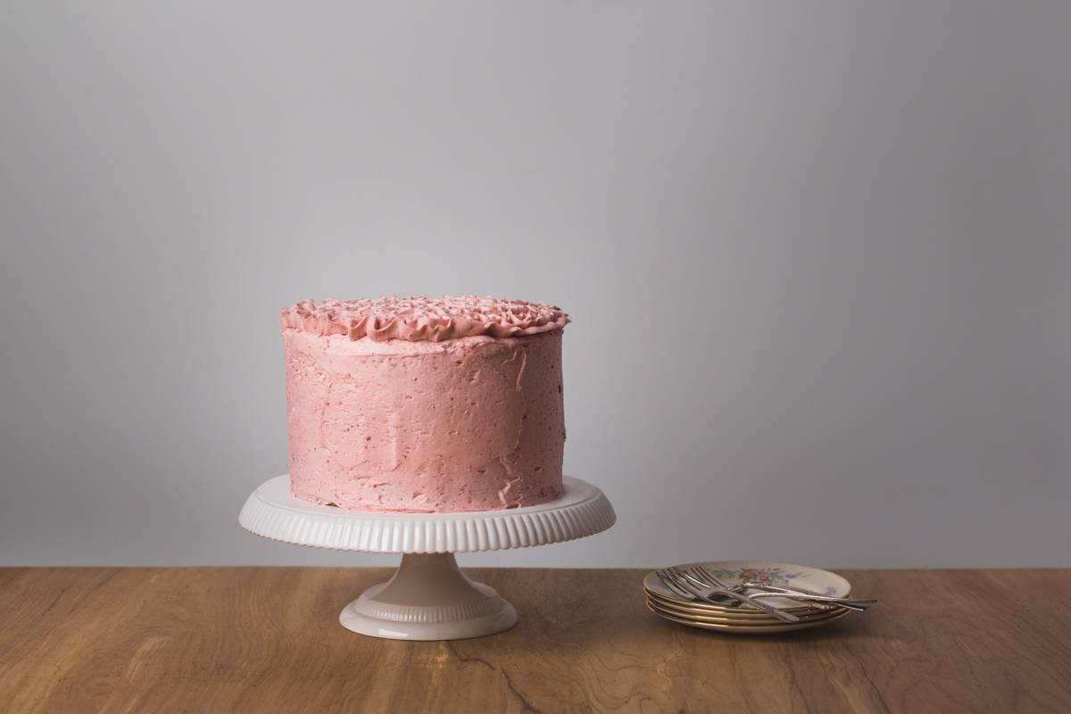 Strawberry layered cake on white pedestal cake stand.
