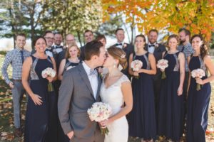 bride and groom kissing in front of wedding party in front of fall colored trees